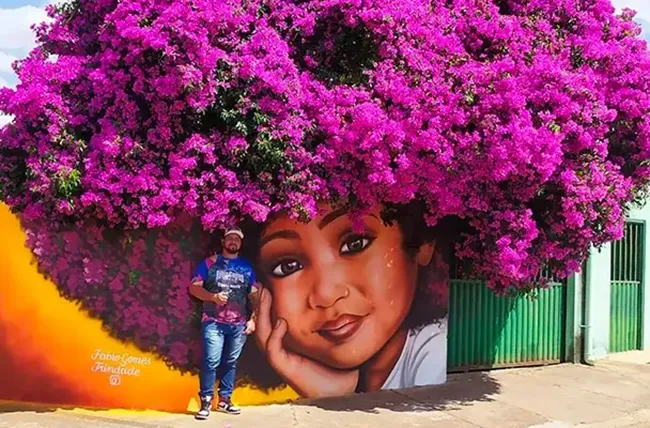 œuvre de Fábio Gomes Trindade, graffiti d’une enfant aux cheveux violets faits par un arbre fleuri